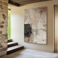 an abstract painting hangs on the wall next to some stone steps in a room with white walls