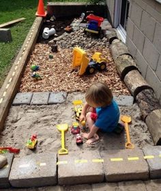 a little boy playing in the sand with toys and construction equipment on his back yard