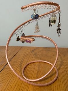 a copper wire sculpture with jewelry hanging from it's sides on a wooden table