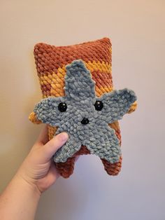 a hand holding up a crocheted starfish pillow