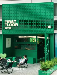 two people sitting in lawn chairs outside the first floor coffee shop, with green walls