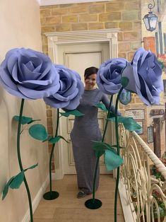 a woman standing next to three giant blue roses