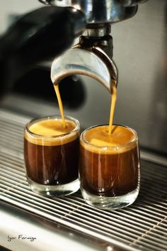 two glasses filled with liquid being poured into each other on top of a metal table