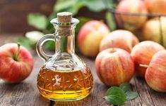 an apple cider sitting on top of a wooden table with apples in the background