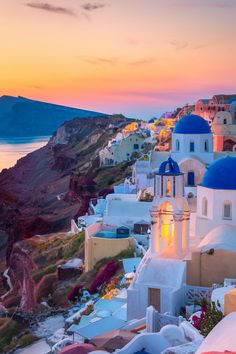 the sun is setting over some white buildings with blue domes on them, overlooking the ocean