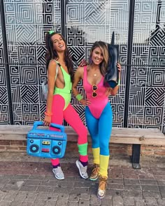 two women in colorful outfits standing next to each other on a brick sidewalk with a boombox