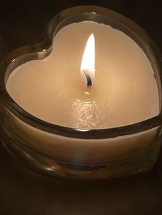 a heart shaped candle sitting on top of a glass container with a lit candle in it