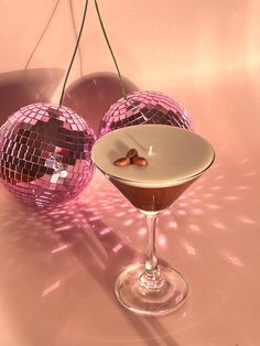 two martini glasses filled with liquid sitting on a pink counter top next to disco balls