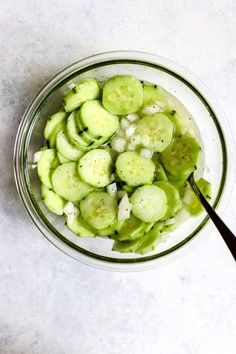 a glass bowl filled with cucumbers on top of a white counter next to a spoon