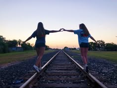 two girls standing on train tracks with their hands in each other's heart shape