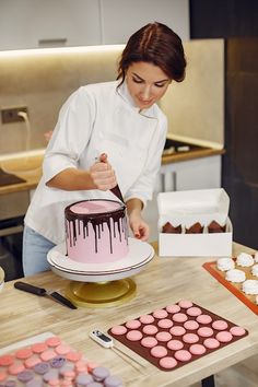 a woman is decorating a cake with chocolate icing on the table next to cupcakes