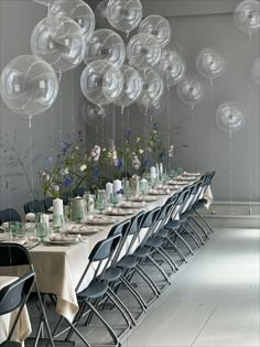 a long table with many clear balloons hanging from it's ceiling and chairs around it