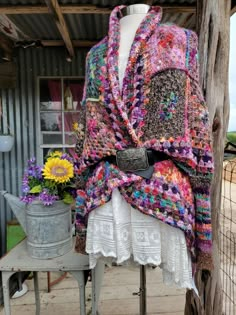 a crocheted shawl draped over a mannequin with flowers in the background