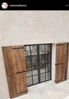 two wooden doors are open in front of a white stucco building with stone floors and windows