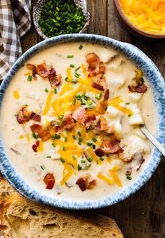 a bowl of potato soup with bacon, cheese and bread on a wooden table top