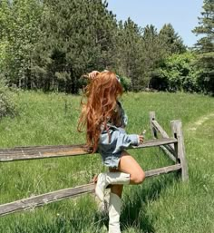 a woman leaning on a wooden fence in the grass