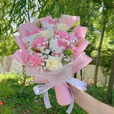 a person holding a pink and white bouquet with hello kitty on the top, in front of a tree