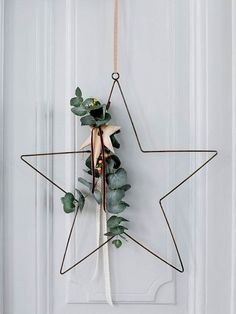 a star decoration hanging on a door with eucalyptus leaves and other greenery attached to it