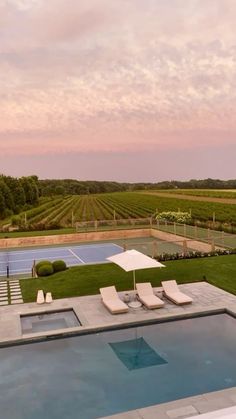 an outdoor swimming pool with lounge chairs next to it and a tennis court in the background