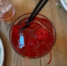 a red drink with two black straws in it on top of a wooden table