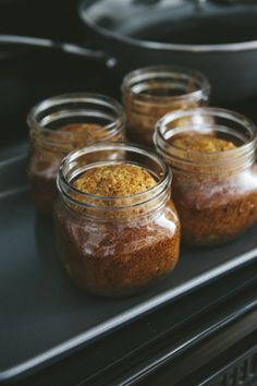 four jars filled with food sitting on top of a stove