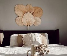 a white bed topped with pillows and a vase filled with dried flowers next to it