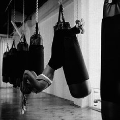 black and white photograph of a person hanging upside down in a gym with punching gloves