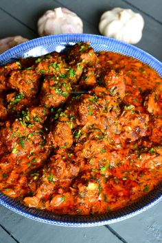 a blue bowl filled with meatballs and sauce on top of a table next to garlic