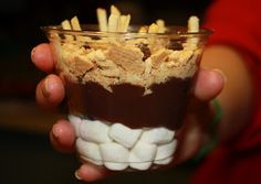 a person holding a small cup filled with marshmallows and chocolate pudding in it