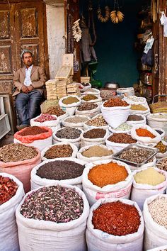 a man sitting in front of bags filled with different types of spices and grains on display