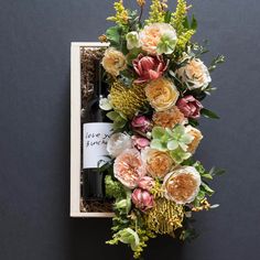 an arrangement of flowers and greenery in a wooden box with a bottle of wine