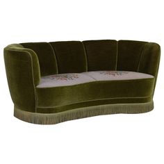 a green couch with white pillows and fringe trimming on the armrests, sitting in front of a white background