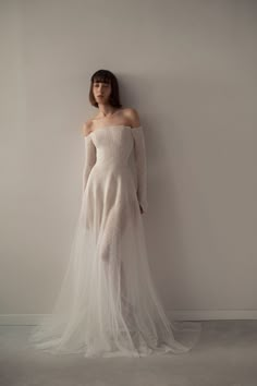 a woman in a white dress standing against a wall