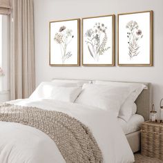 a bedroom with white bedding and two paintings on the wall