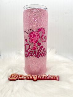 a pink glitter tumbler sitting on top of a white fur covered floor next to a candy bar