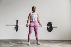 a woman holding a barbell while standing in front of a white wall