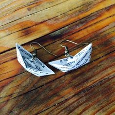 two origami boats are sitting on top of a wooden table with earrings hanging from them