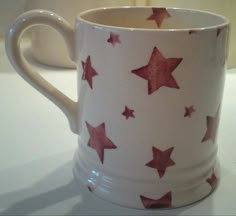 a coffee cup with red stars on it sitting on a white counter top next to a candle