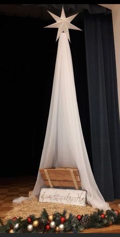 a christmas decoration with a star above it on top of a wooden crate in front of a curtain