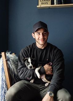 a man sitting on a chair holding a small dog in his lap and smiling at the camera