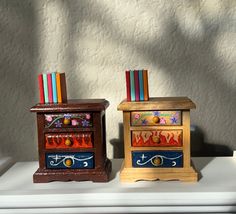 two wooden boxes with painted designs on them sitting on a shelf next to each other