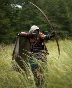 a man dressed in medieval clothing holding a bow and arrow while standing in tall grass