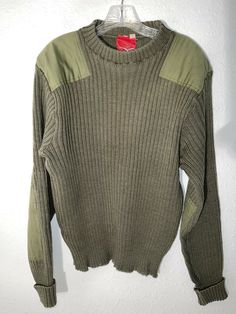 a green sweater hanging on a white wall with a red tag attached to the front