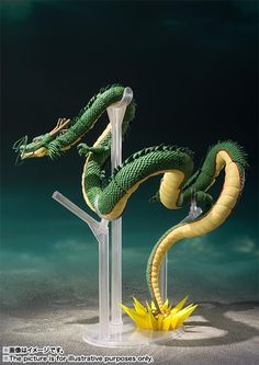 a green and yellow dragon figurine sitting on top of a glass stand in the sand