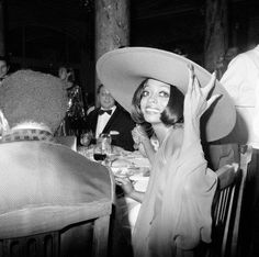 a woman wearing a large hat sitting at a table with other people in the background