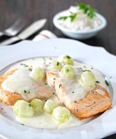 a white plate topped with fish covered in gravy and garnished with peas