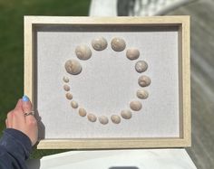 a person holding up a framed artwork with seashells arranged in the shape of a heart