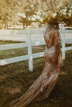 a woman standing in front of a white fence wearing a long dress and black hat