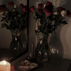 two vases filled with roses sitting on top of a table next to a candle