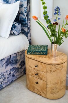 a vase with flowers sitting on top of a wooden dresser next to a blue and white bed